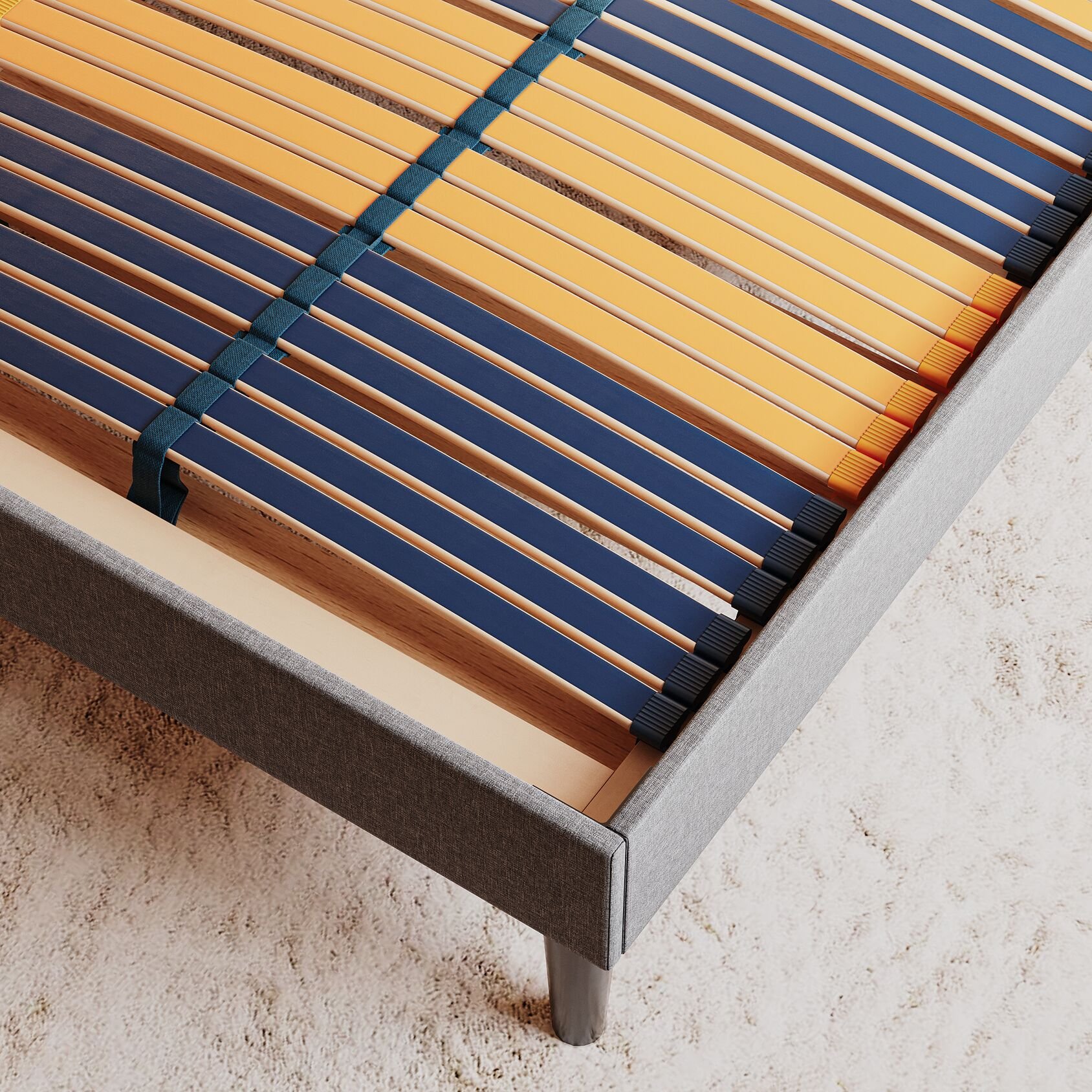 Primo piano di una rete letto con doghe in legno e bordo imbottito grigio, su tappeto chiaro