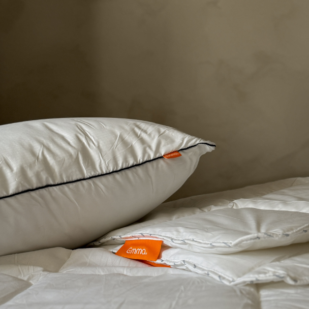 Wit beddengoed met een kussen en een opgevouwen dekbed met oranje label op een bed tegen een neutrale muur