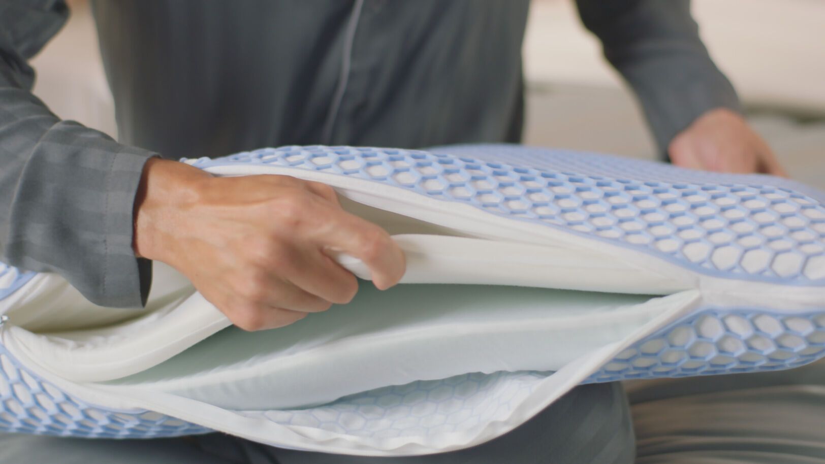 Persoon in geruit shirt opent AirGrid® Adapt Kussens met blauw hexagonaal raster; binnenlagen zichtbaar in doorsnede.