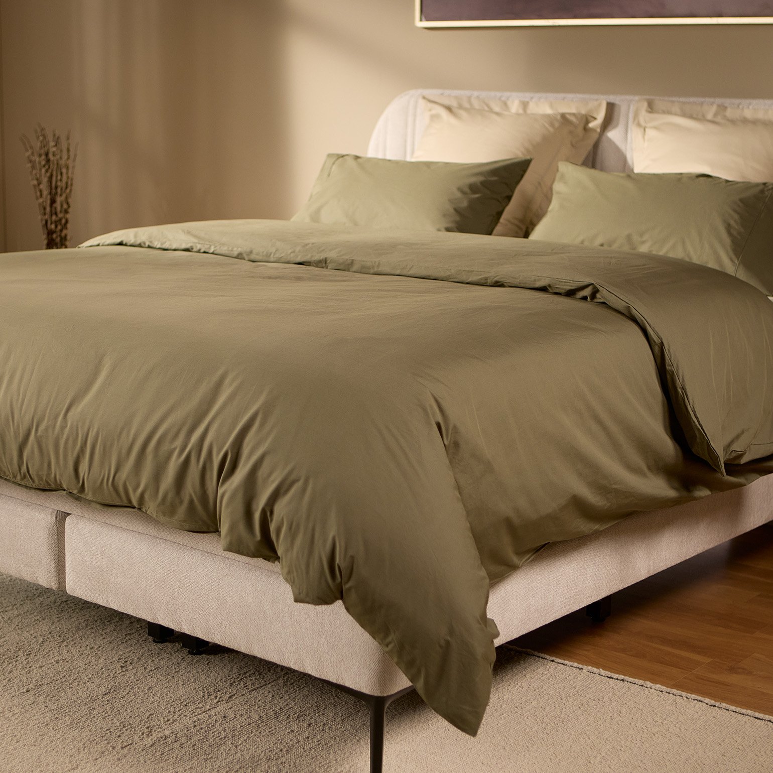 Emma Boxspring Bed in beige with curved channelled headboard styled with olive green bedding in a warm bedroom.
