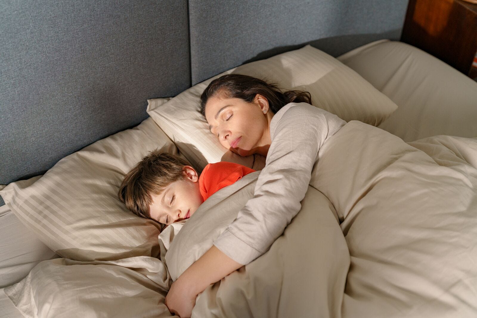 mujer y niño en la cama arropados con un edredon durmiendo juntos