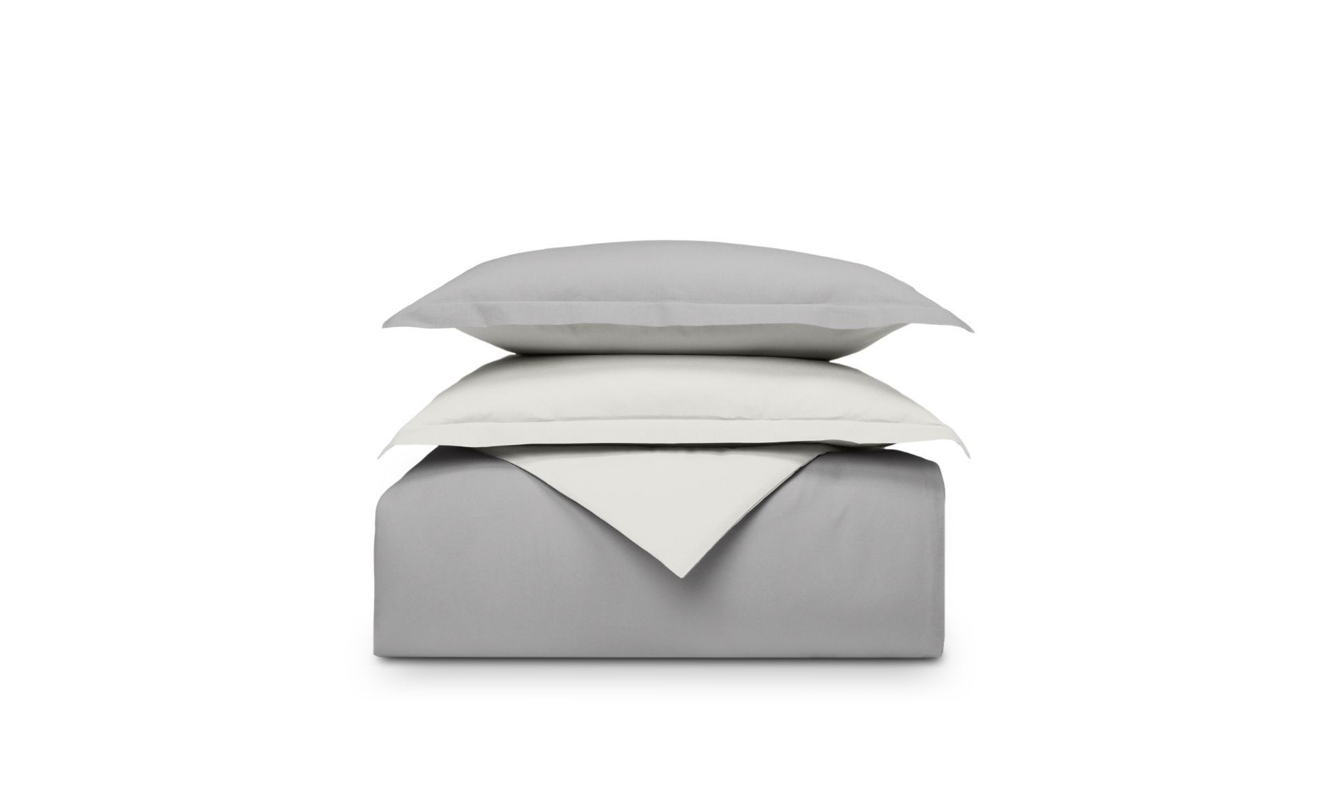 Set di biancheria piegato grigio e bianco sfondo bianco, cuscino sopra il piumone.