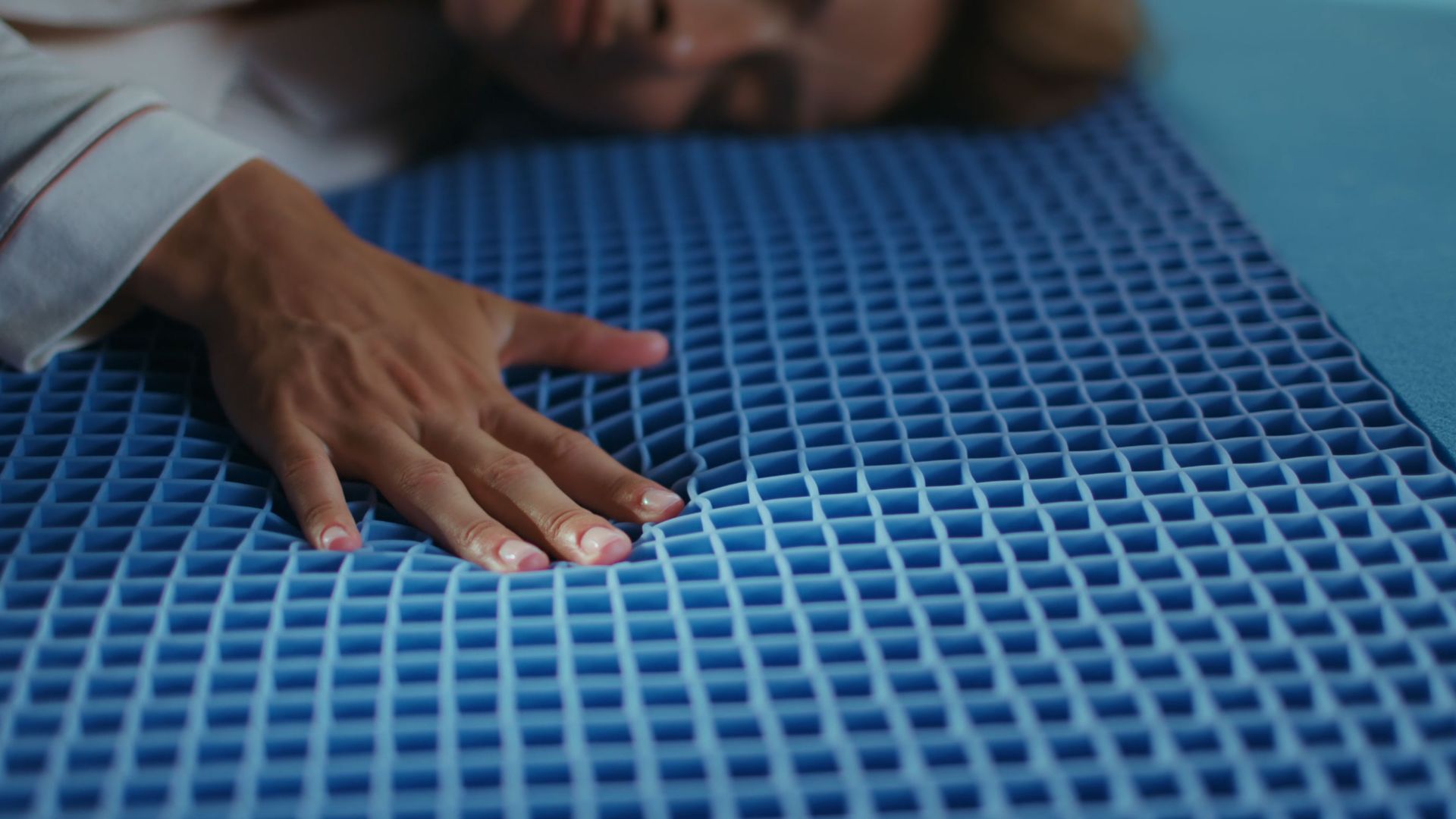 Hand pressing into the blue grid foam layer of the Emma Original Elite mattress, showing its open-cell structure in close-up detail.