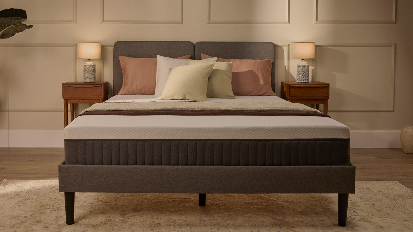 Lit tapissé gris avec matelas blanc, dans une chambre.