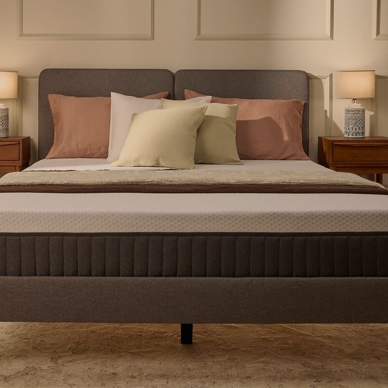 Lit tapissé gris avec matelas blanc, dans une chambre.