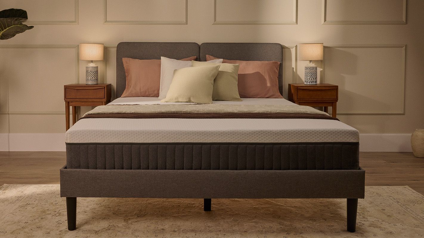 Lit tapissé gris avec matelas blanc, dans une chambre.