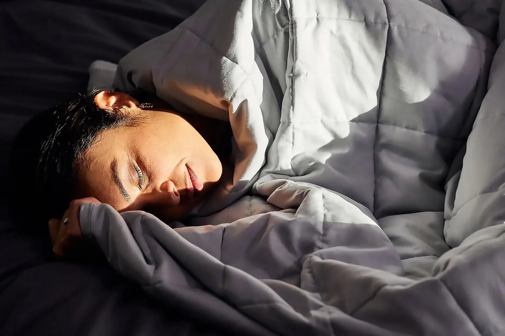 Persoon rust in bed onder een Emma Hug verzwaringsdeken, gezicht zacht verlicht door zonlicht dat door een nabijgelegen raam valt.