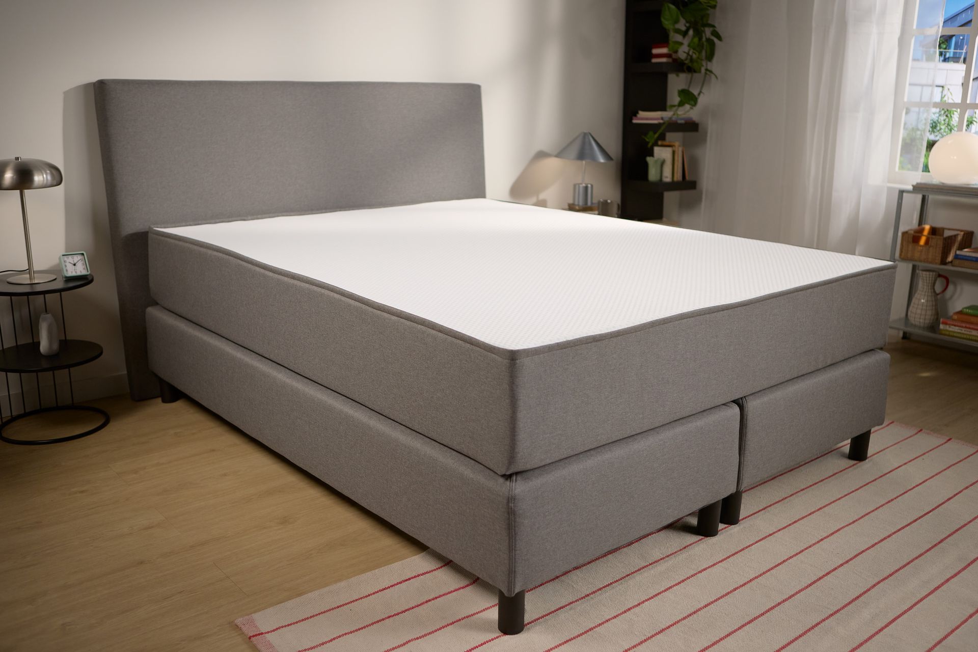 Schuin aanzicht met de gestoffeerde basis, de diepte van het hoofdbord en twee centrale steunpoten voor extra stabiliteit.