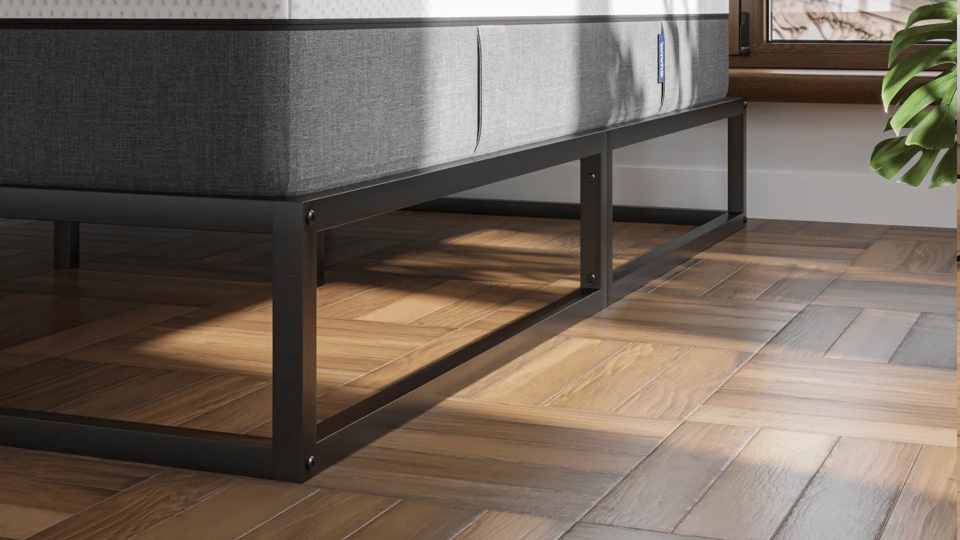 Minimalistisch metalen bedframe in zwarte afwerking, geplaatst op visgraat houten vloer; bed is voorzien van wit matras met grijze zijpanelen en staat voor raam met uitzicht op dakpannen en een groene plant in de hoek.
