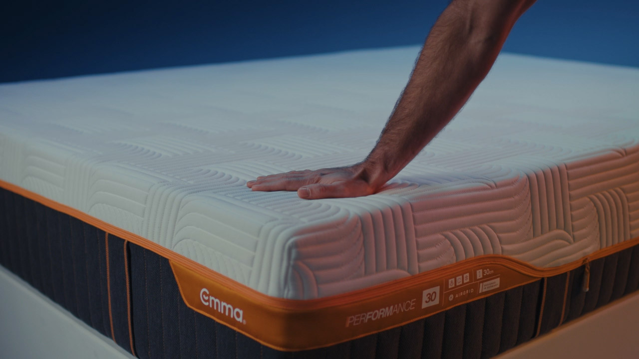Hand firmly pressing on the corner of an Emma Performance mattress, illustrating its firmness.