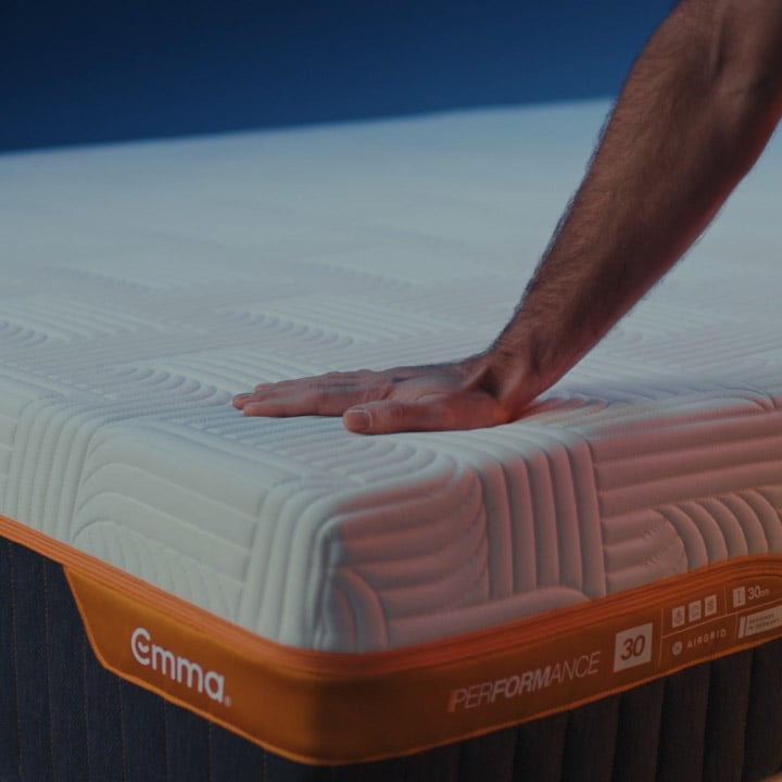 Hand firmly pressing on the corner of an Emma Performance mattress, illustrating its firmness.