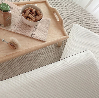Houten dienblad met schaal met gedroogd fruit, borstel en fles op een Emma matras naast twee Emma Diamond kussens.