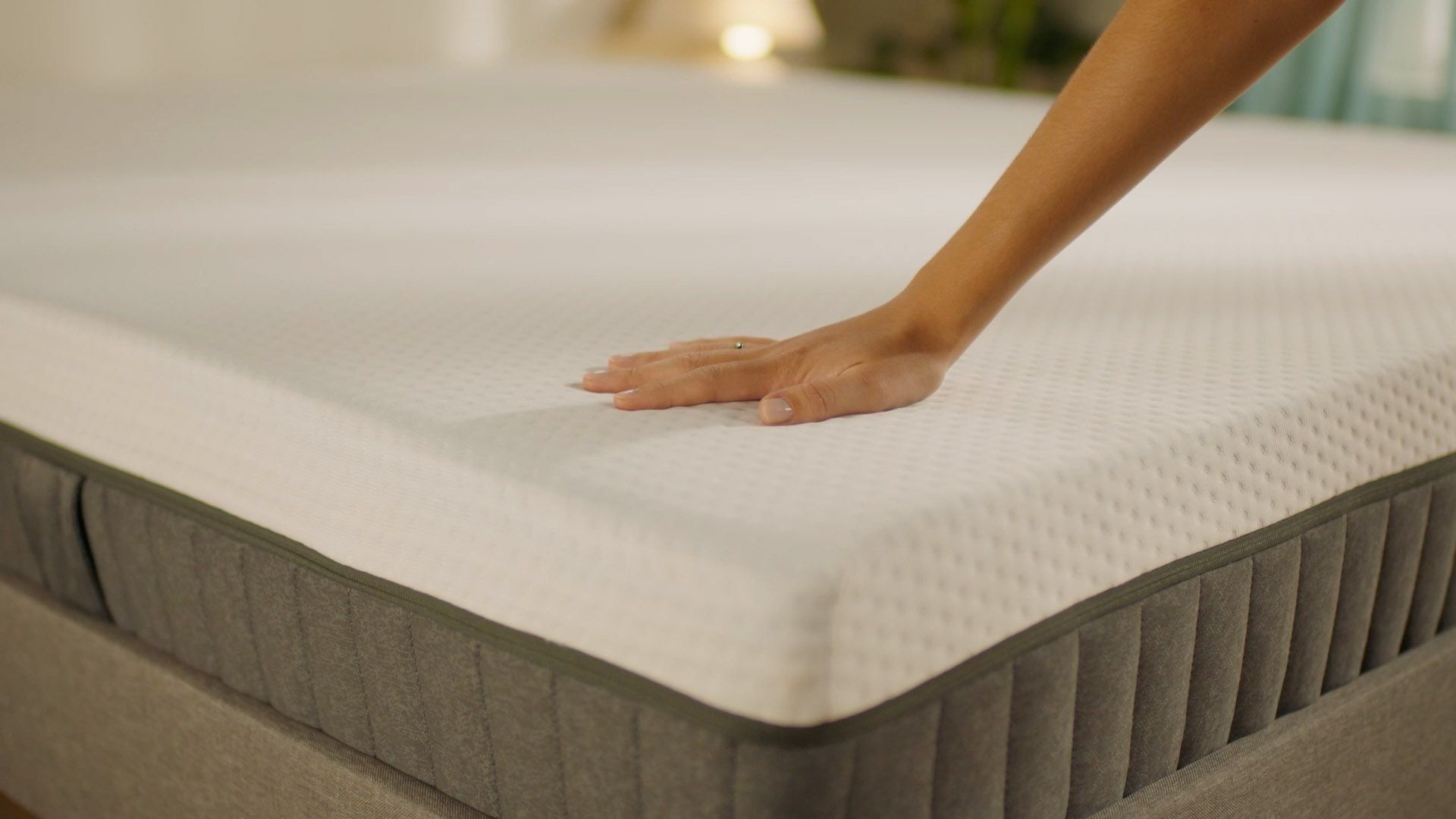 Main testant la fermeté d’un matelas en mousse à mémoire de forme sur un matelas gris