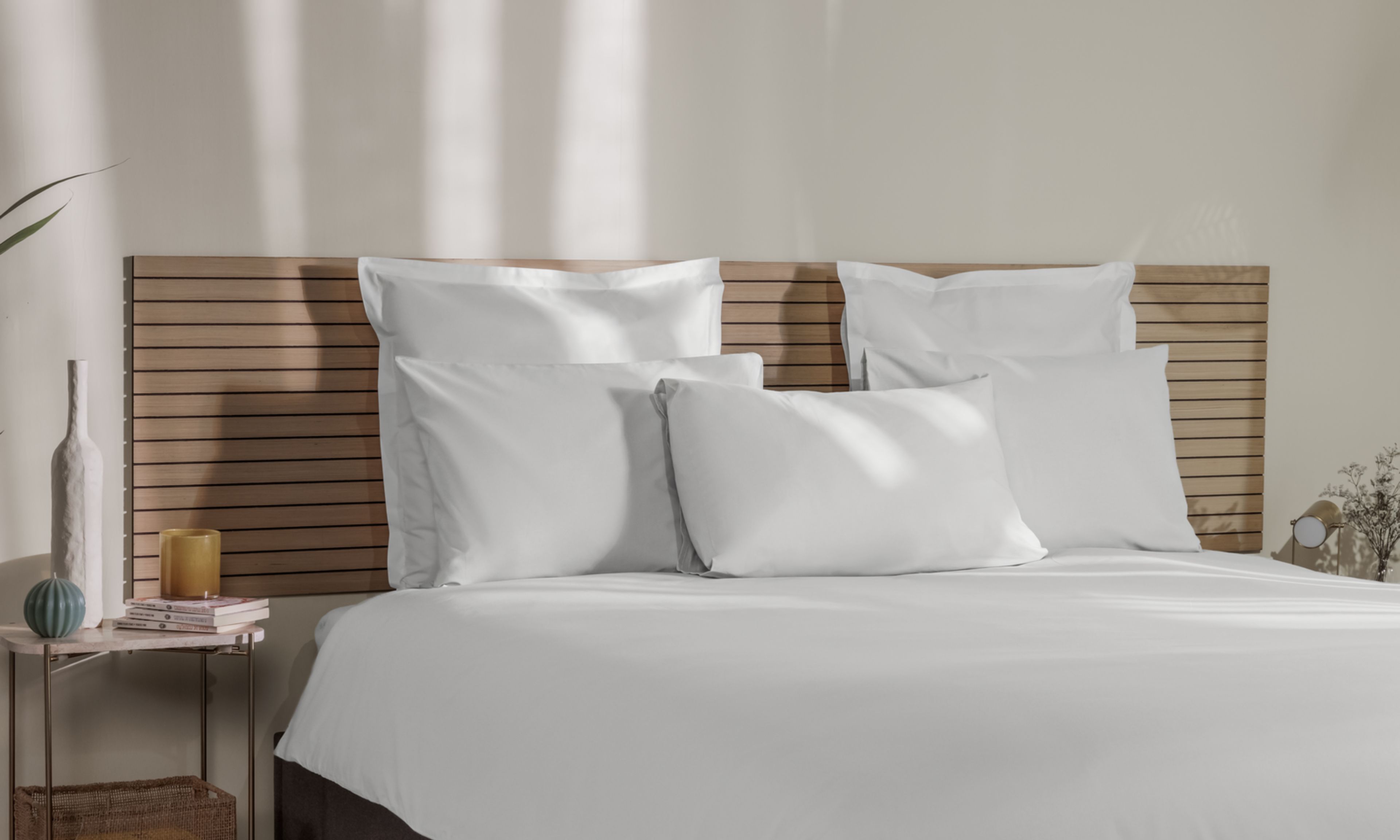 Letto con federe bianche, copripiumino coordinato e testiera in legno.