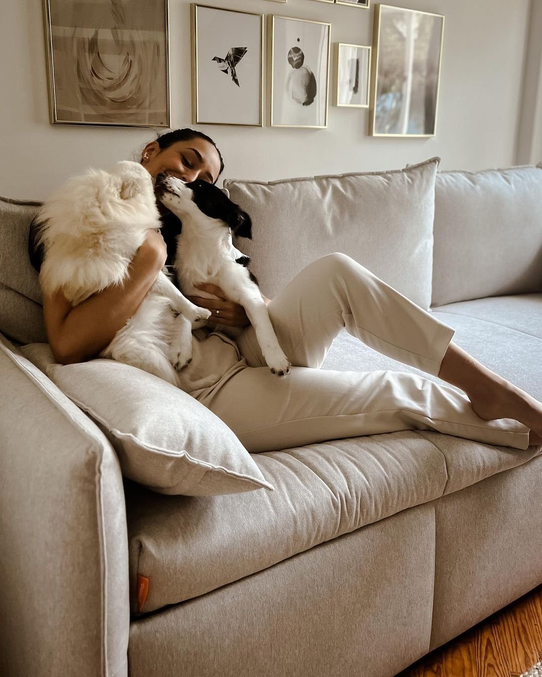 Mulher sentada num Sofá Cama beige Emma abraçada a dois cães