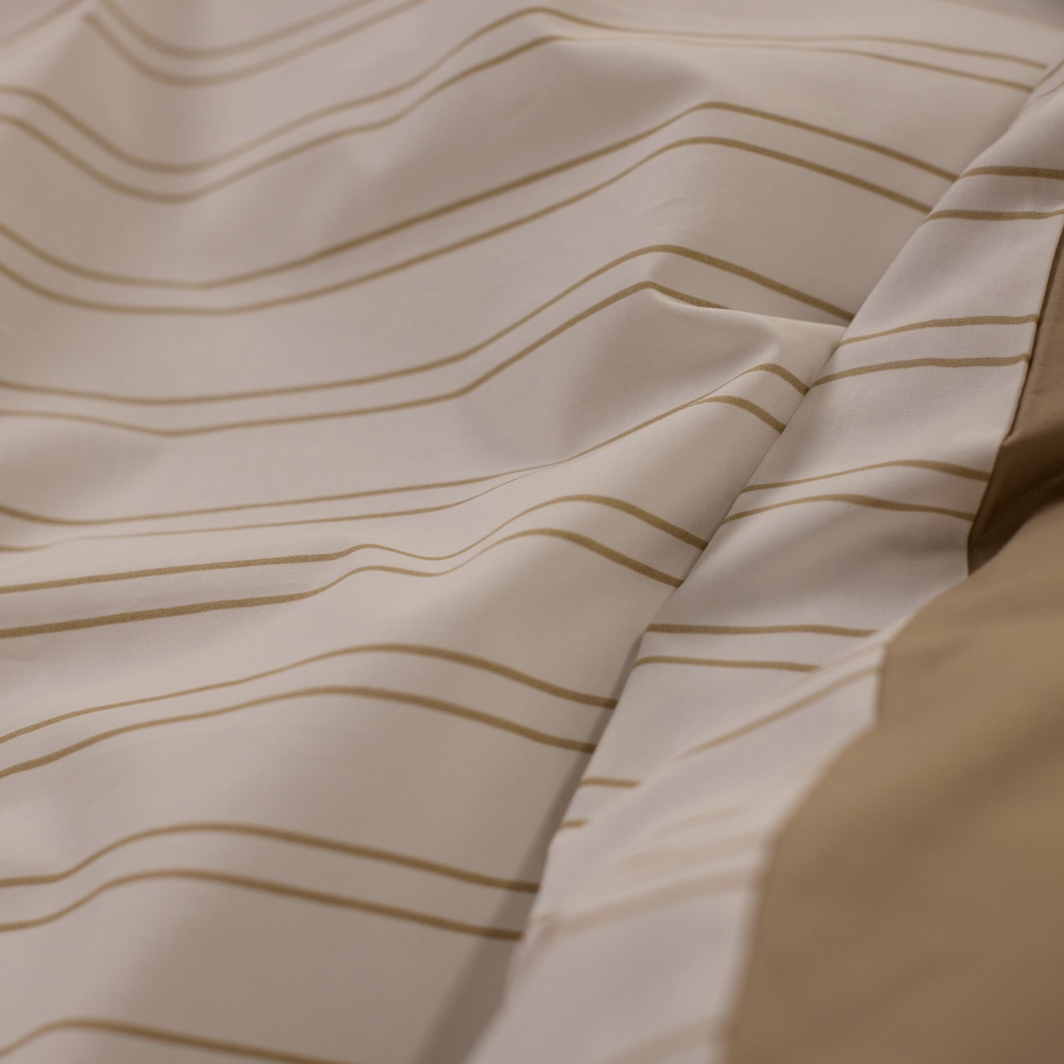 Close‑up van beige en wit beddengoed met een subtiel gestreept patroon.