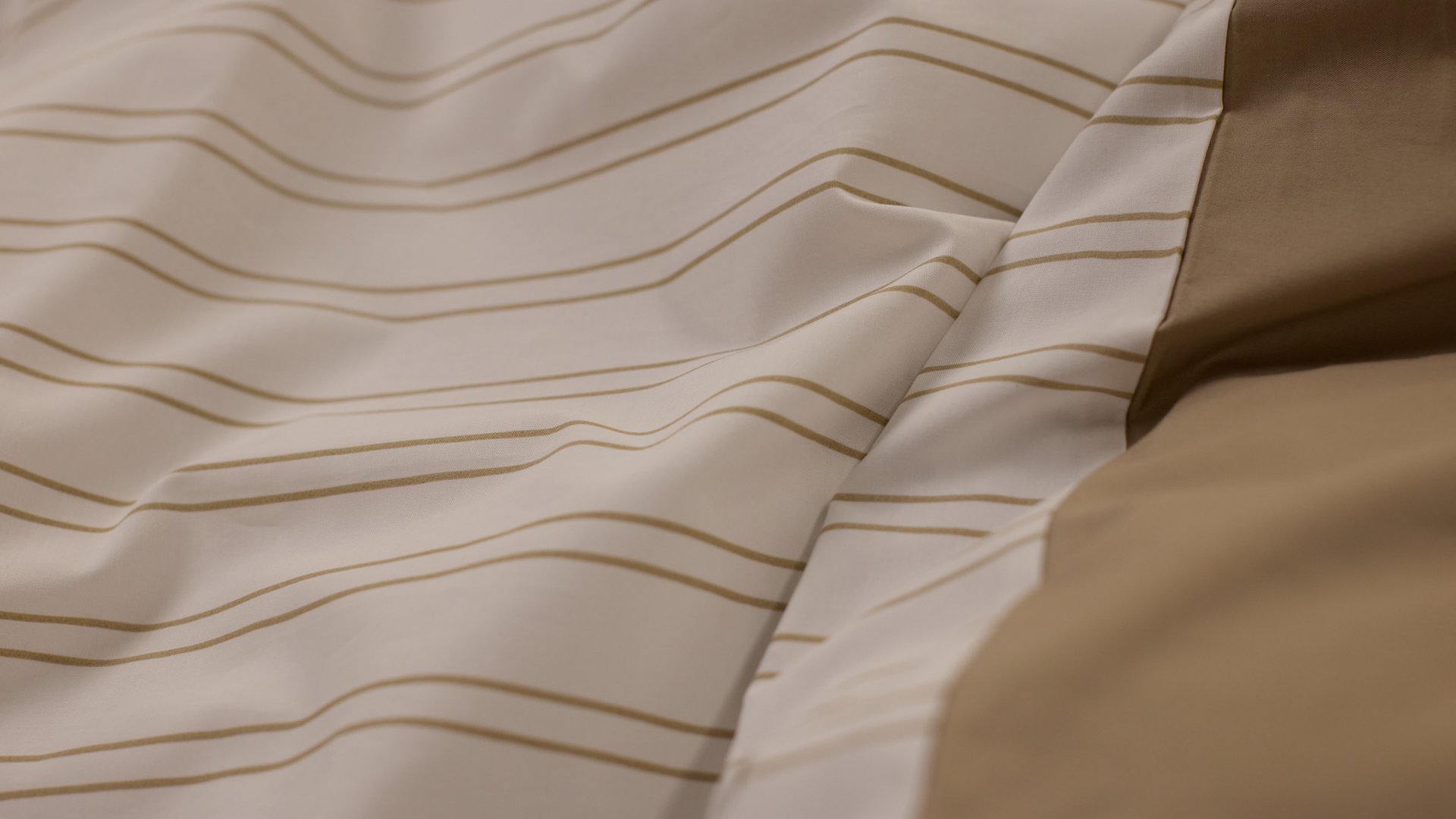 Close‑up van beige en wit beddengoed met een subtiel gestreept patroon.