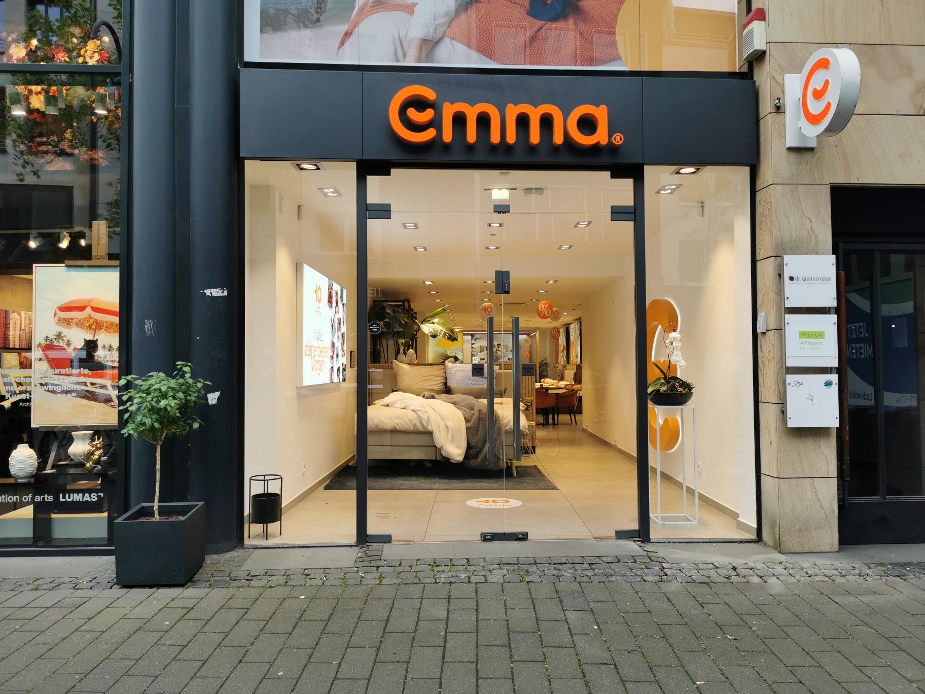 Emma Store Köln, schwarze Fassade, großes orangefarbenes Emma-Logo, Eingang mit Glasfront.