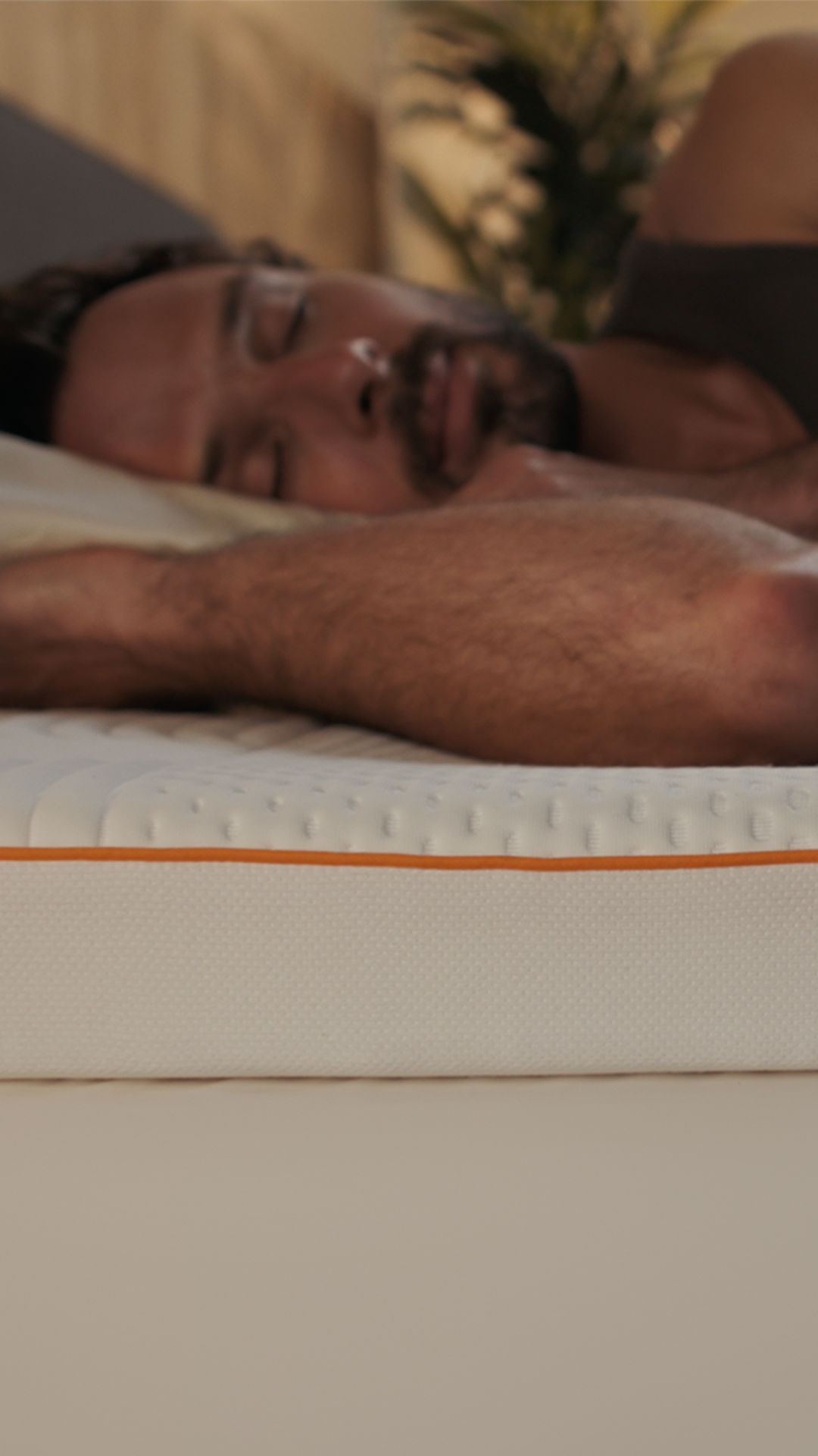 Man sleeping on Emma Performance Topper with quilted white surface and orange stripe detail.