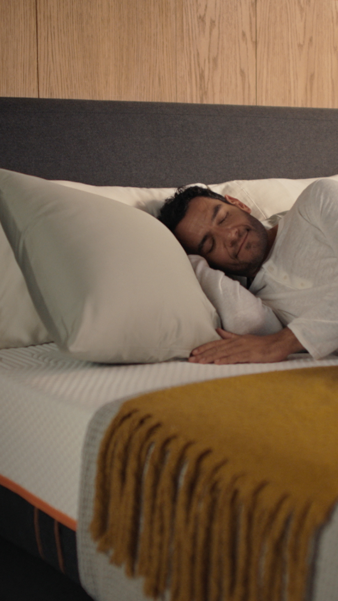 Een man die slaapt op een Emma Performance-boxspringbed met een in antraciet bekleed hoofdeinde in een gezellige slaapkamer.