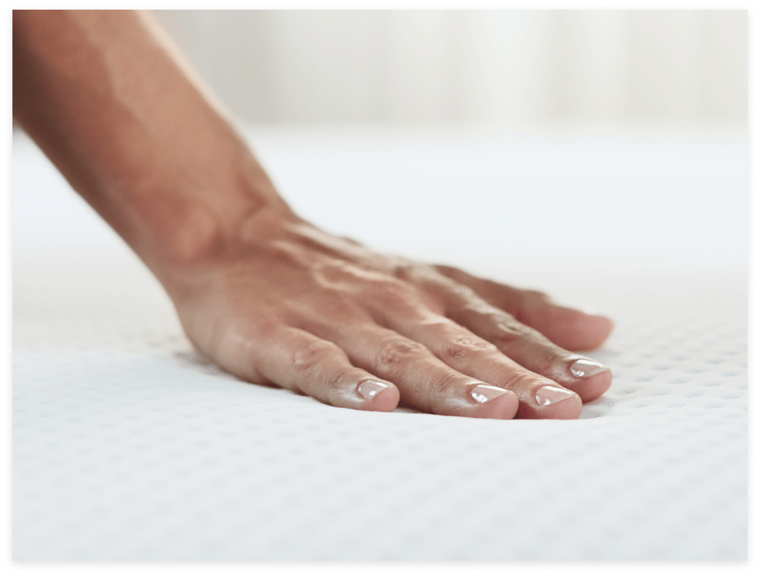 Gros plan d'une main appuyant sur la surface d'un matelas blanc et texturé, montrant la légère indentation et la douceur du matelas.