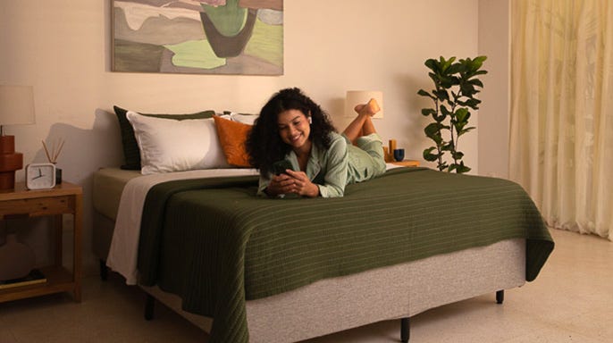 Femme allongée détendue sur un lit Emma avec du linge de lit à rayures vertes dans une chambre aménagée de façon moderne.
