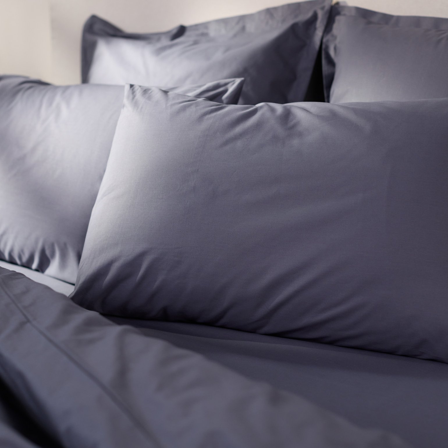 Close‑up van een opgemaakt bed met donkergrijs beddengoed en meerdere kussens in dezelfde tint.