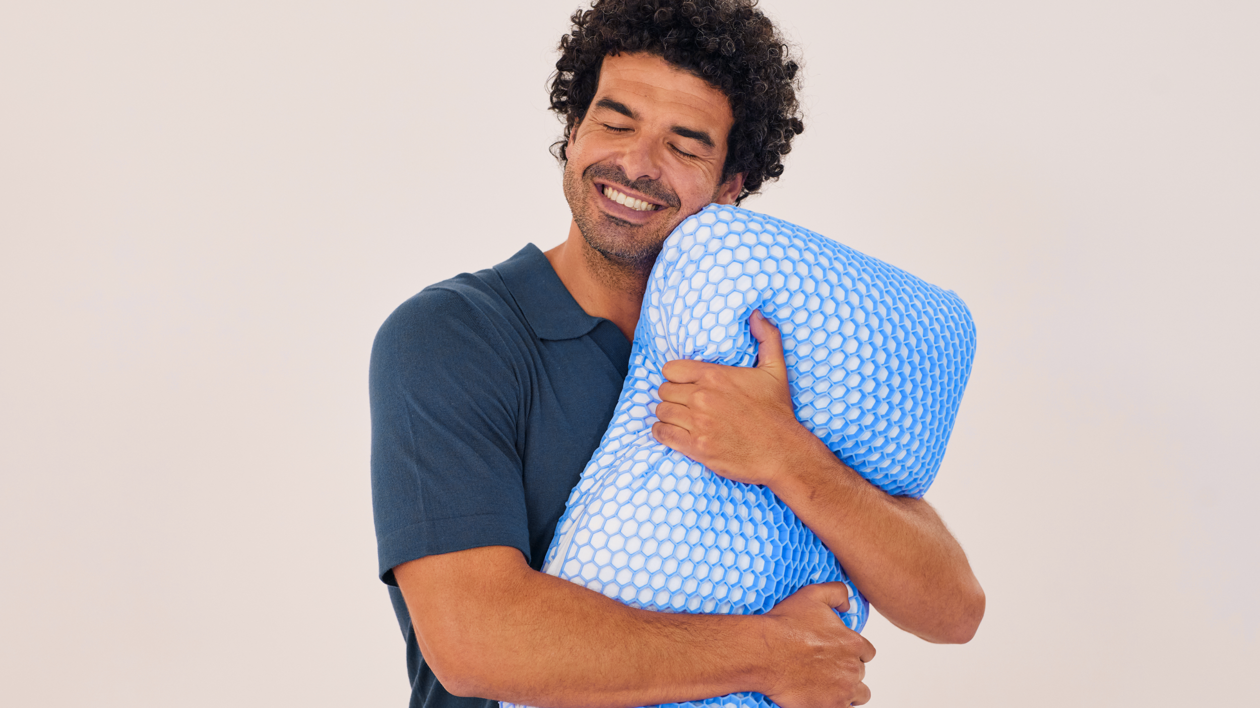 Homme portant une chemise bleu foncé, serrant un oreiller avec une grille en forme de nid d’abeille bleue.