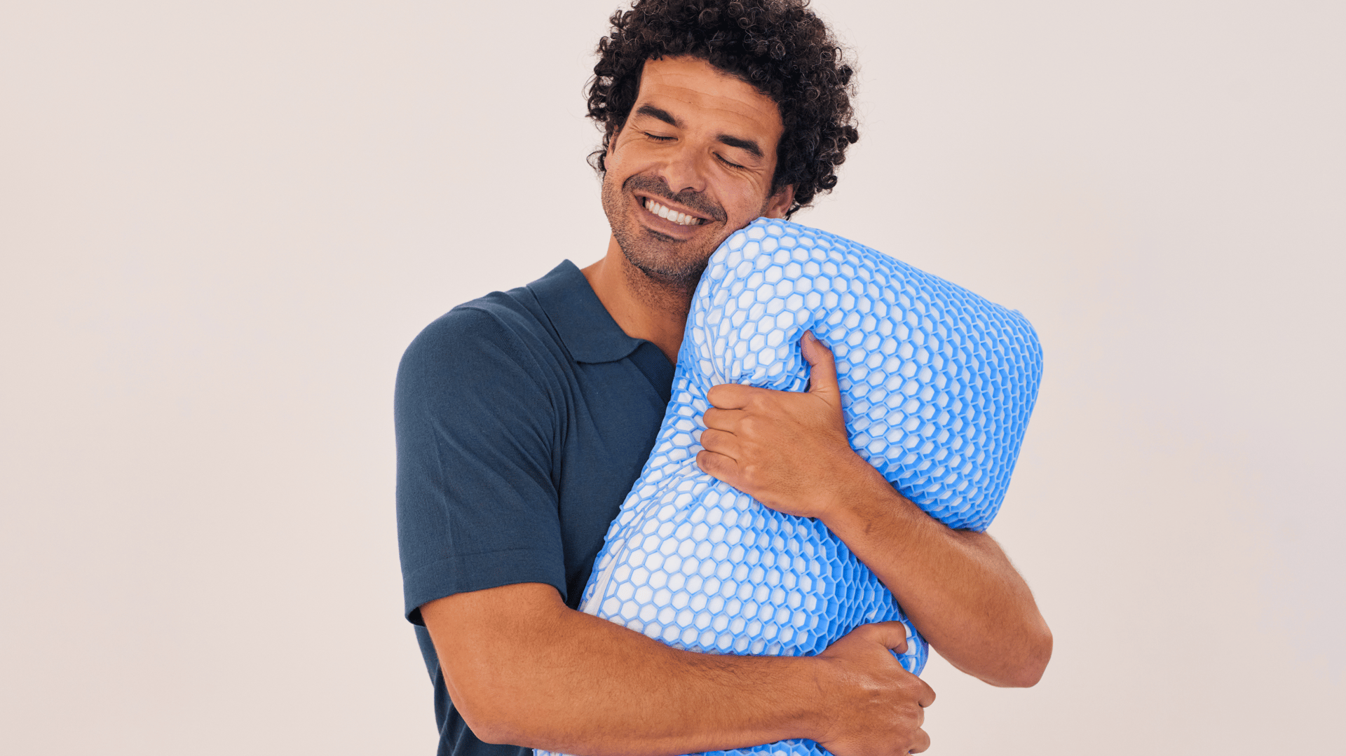 Homme portant une chemise bleu foncé, serrant un oreiller avec une grille en forme de nid d’abeille bleue.