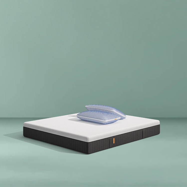 Lit moderne avec tête de lit grise et pieds noirs, recouvert de draps blancs. Deux oreillers blancs et une pile de linge plié sont posés sur le matelas. Arrière-plan beige avec une forme orange abstraite.