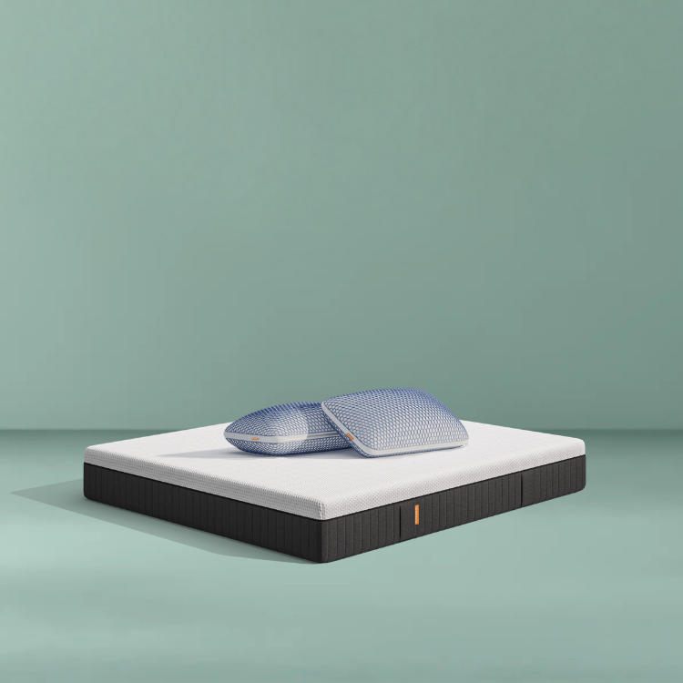 Lit moderne avec tête de lit grise et pieds noirs, recouvert de draps blancs. Deux oreillers blancs et une pile de linge plié sont posés sur le matelas. Arrière-plan beige avec une forme orange abstraite.