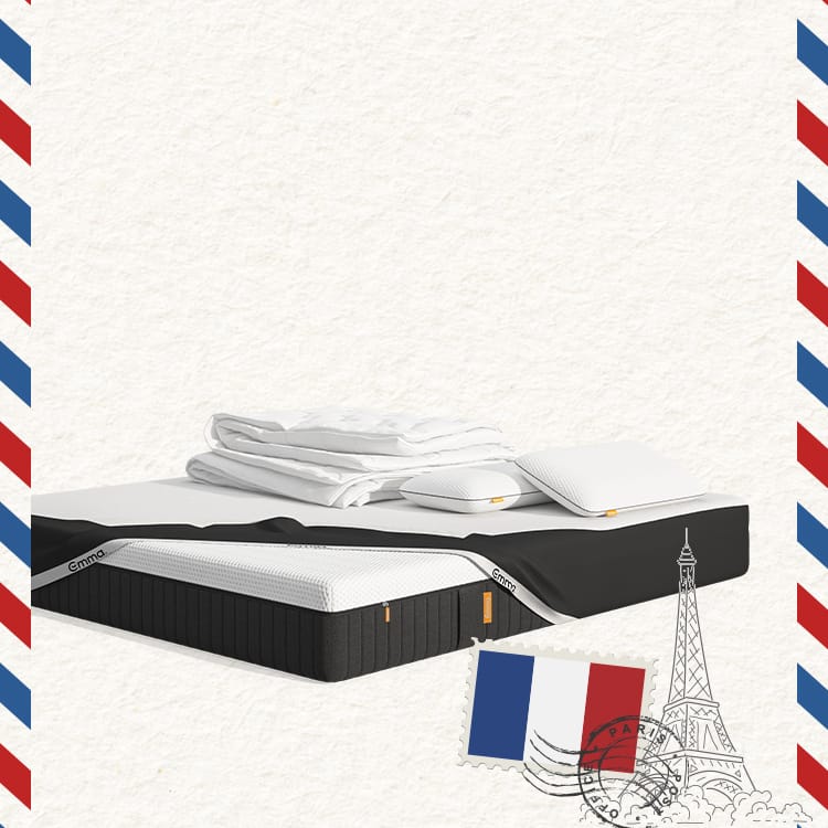 Lit moderne avec tête de lit grise et pieds noirs, recouvert de draps blancs. Deux oreillers blancs et une pile de linge plié sont posés sur le matelas. Arrière-plan beige avec une forme orange abstraite.