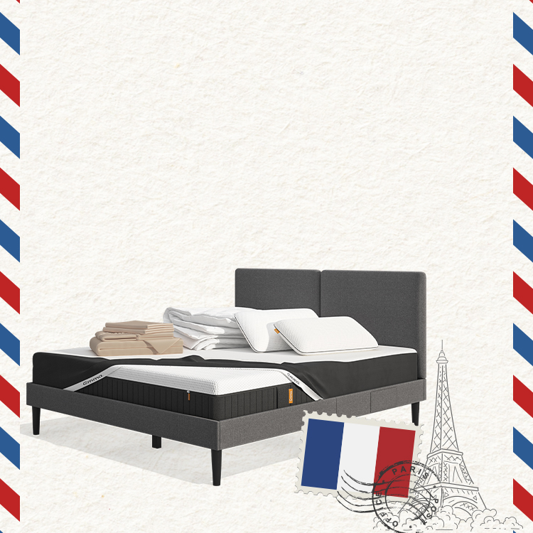 Lit moderne avec tête de lit grise et pieds noirs, recouvert de draps blancs. Deux oreillers blancs et une pile de linge plié sont posés sur le matelas. Arrière-plan beige avec une forme orange abstraite.