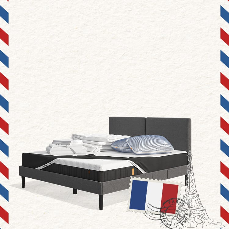 Lit moderne avec tête de lit grise et pieds noirs, recouvert de draps blancs. Deux oreillers blancs et une pile de linge plié sont posés sur le matelas. Arrière-plan beige avec une forme orange abstraite.