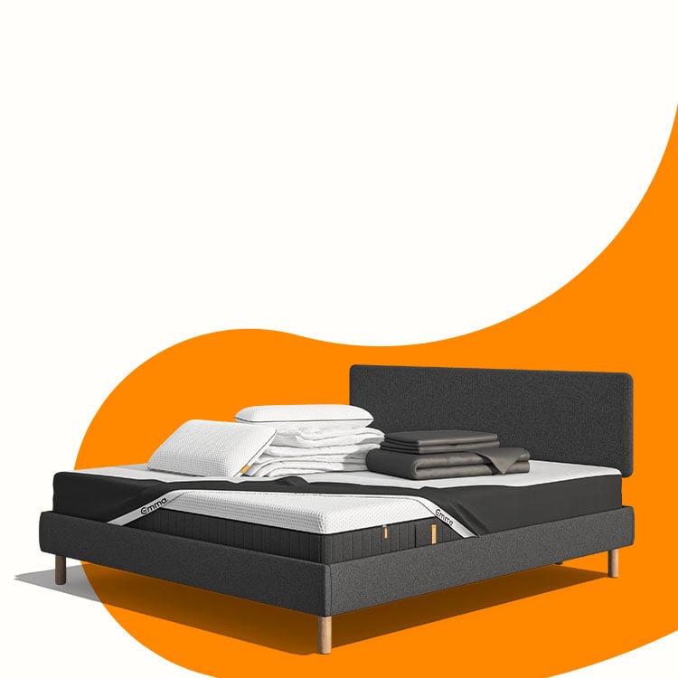 Lit moderne avec tête de lit grise et pieds noirs, recouvert de draps blancs. Deux oreillers blancs et une pile de linge plié sont posés sur le matelas. Arrière-plan beige avec une forme orange abstraite.