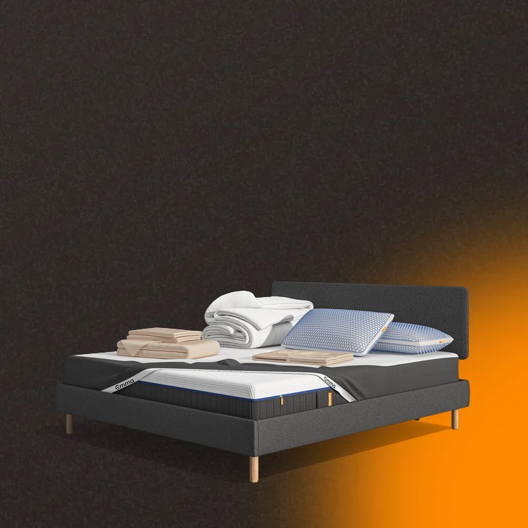 Lit moderne avec tête de lit grise et pieds noirs, recouvert de draps blancs. Deux oreillers blancs et une pile de linge plié sont posés sur le matelas. Arrière-plan beige avec une forme orange abstraite.