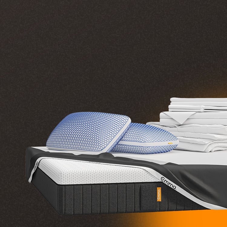 Lit moderne avec tête de lit grise et pieds noirs, recouvert de draps blancs. Deux oreillers blancs et une pile de linge plié sont posés sur le matelas. Arrière-plan beige avec une forme orange abstraite.