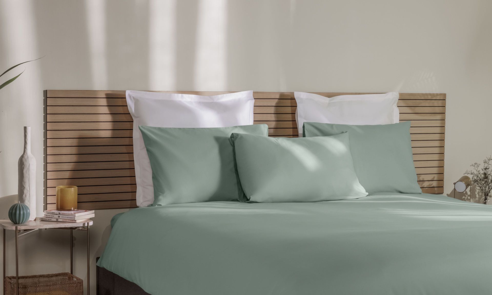 Letto ordinato con biancheria verde e testiera intrecciata.