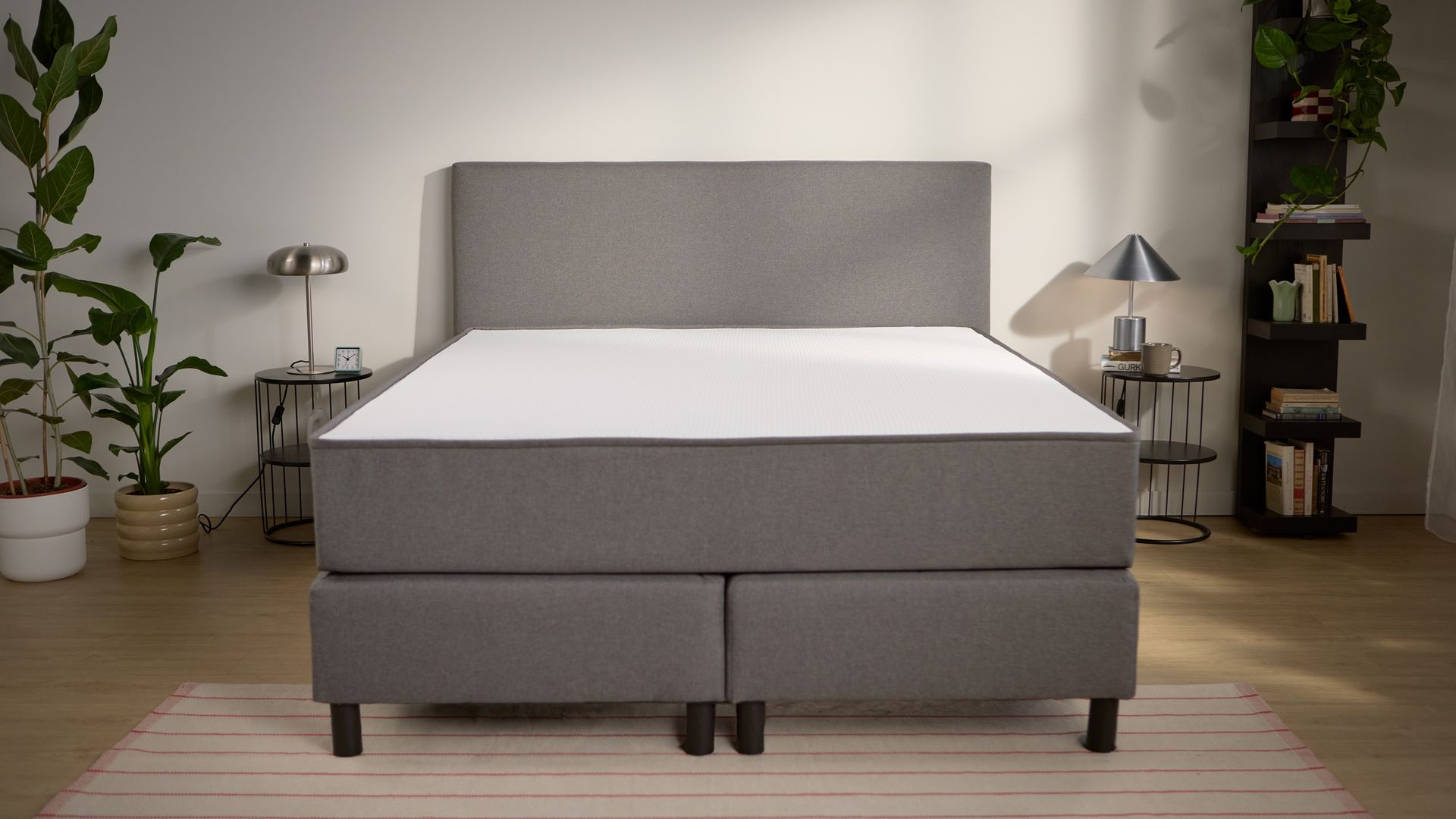 Vooraanzicht van het bed met gestoffeerde boxspringbasis, hoog hoofdbord en gelijkmatig geplaatste steunpoten.