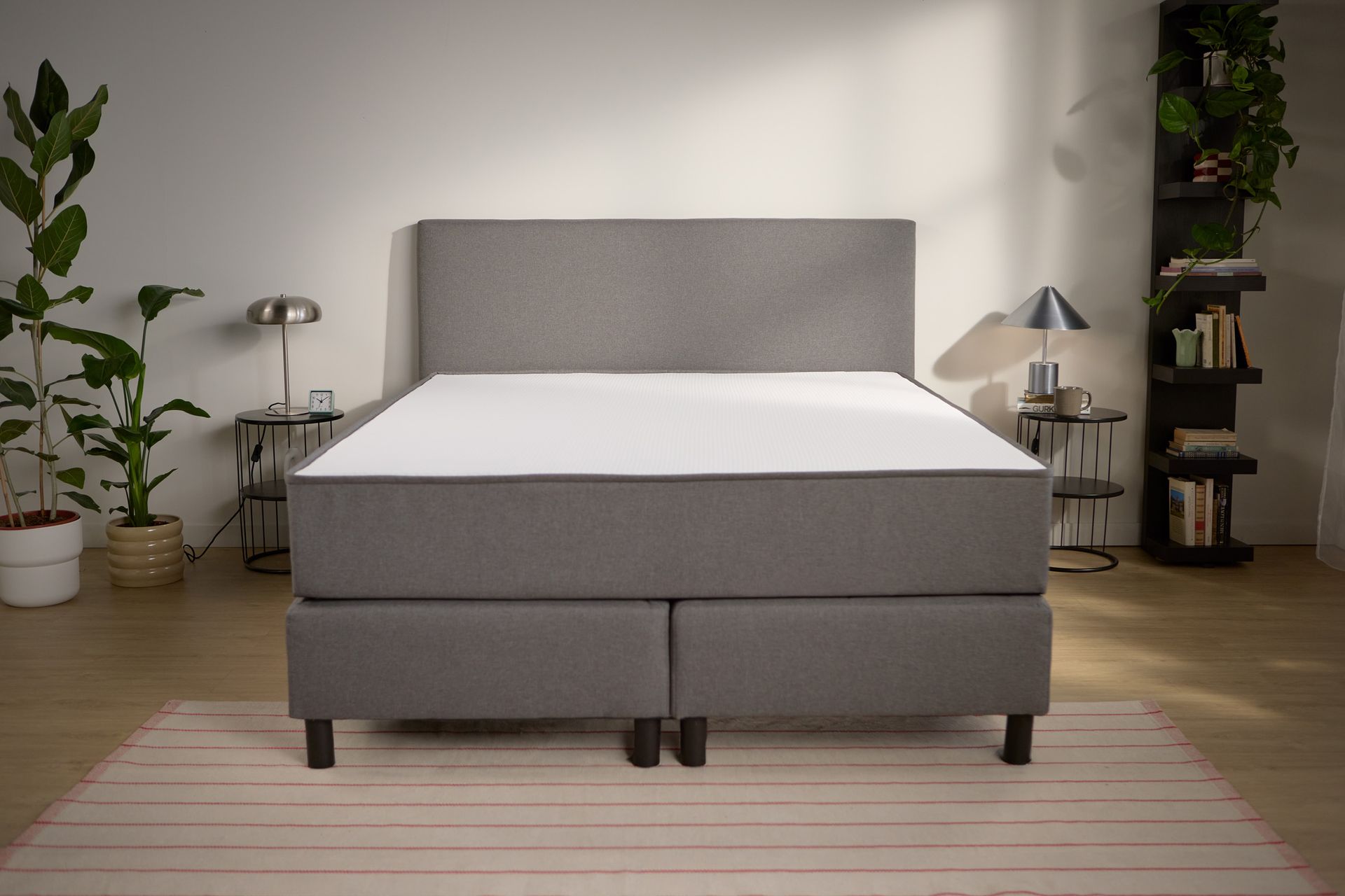 Vooraanzicht van het bed met gestoffeerde boxspringbasis, hoog hoofdbord en gelijkmatig geplaatste steunpoten.