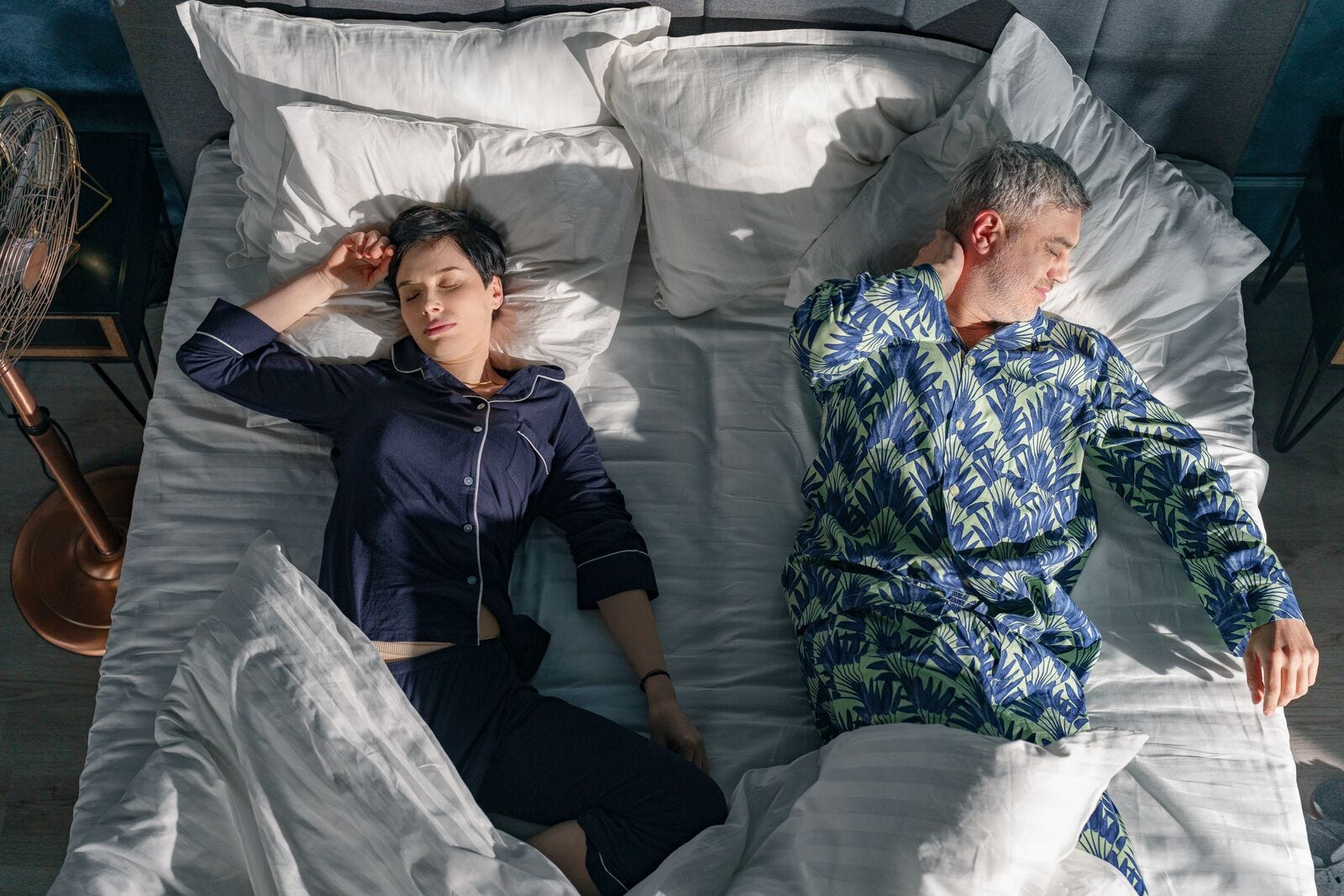 Un chico y una chica durmiento en una cama gris con sbaanas blancas en pijama azul