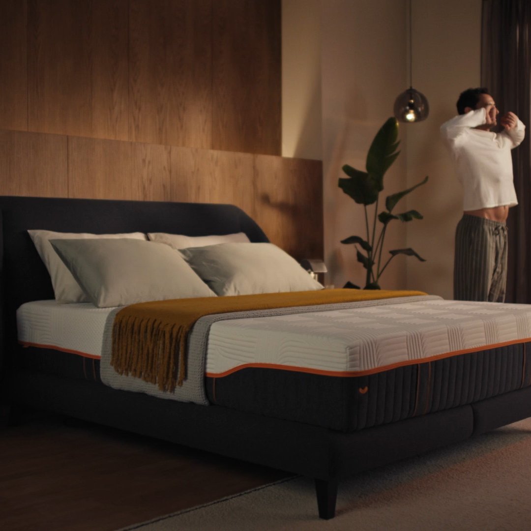 Person stretching after waking next to Emma Performance boxspringbed in a warm, styled bedroom.