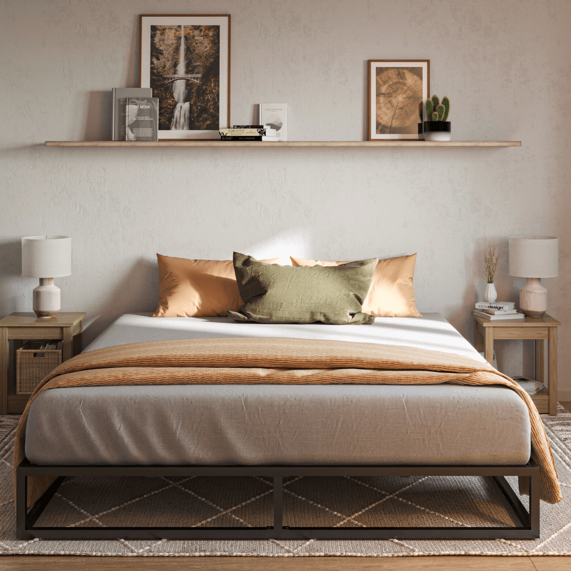 Slaapkamer met grijs gestoffeerd bed, voorzien van oranje plaid en drie kussens (twee oranje, één groen); bed geflankeerd door houten nachtkastjes met decoraties en lampen; boven het bed een wandplank met boeken, foto’s en een cactus; links een grote groene kamerplant, onder bed een beige kleed met geometrisch patroon; rechte grijze gordijnen aan rechterzijde.