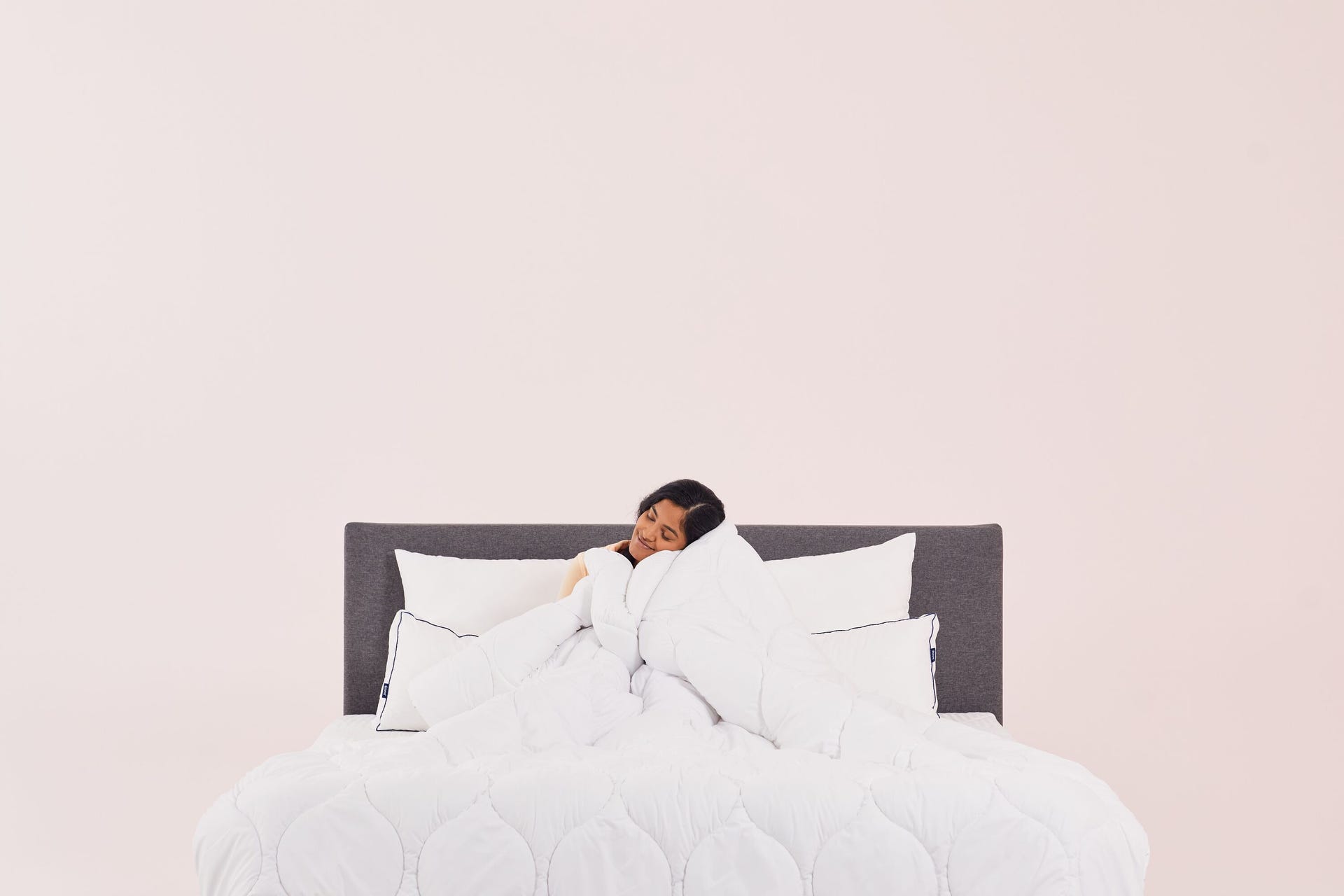 una chica sentada en la cama abraza un edredon blanco