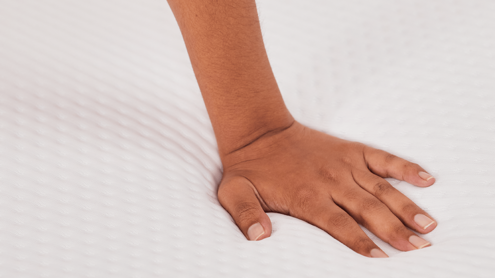 Close-up van een hand die stevig op een witte, gewatteerde bovenlaag van de Emma Original Topper drukt; de indrukbare textuur laat een duidelijke afdruk achter, wat de zachtheid en drukverlagende eigenschappen van het materiaal benadrukt.