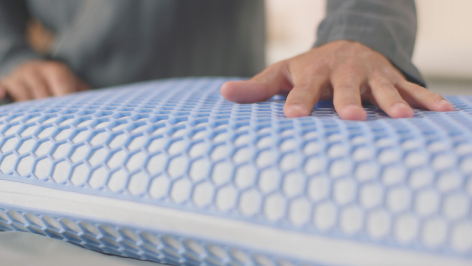Hand drukt op Emma AirGrid® Kussen met blauw hexagonaal raster en witte onderlaag; textuur en veerkracht zichtbaar.