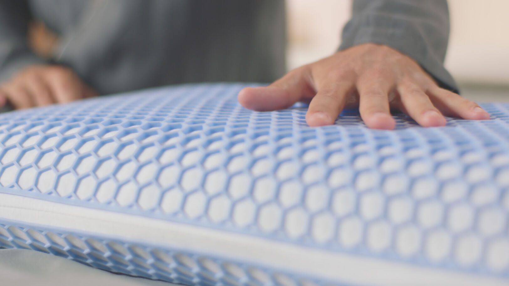 Hand drukt op AirGrid® Adapt Kussens met blauw hexagonaal raster en witte onderlaag; textuur en veerkracht zichtbaar.