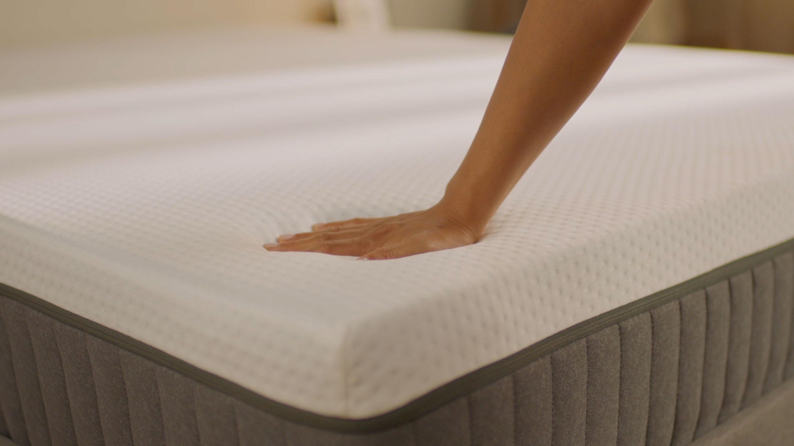 Hand die zacht op de bovenlaag van een Emma Original‑matras drukt om het comfort en de drukverlichting te tonen.