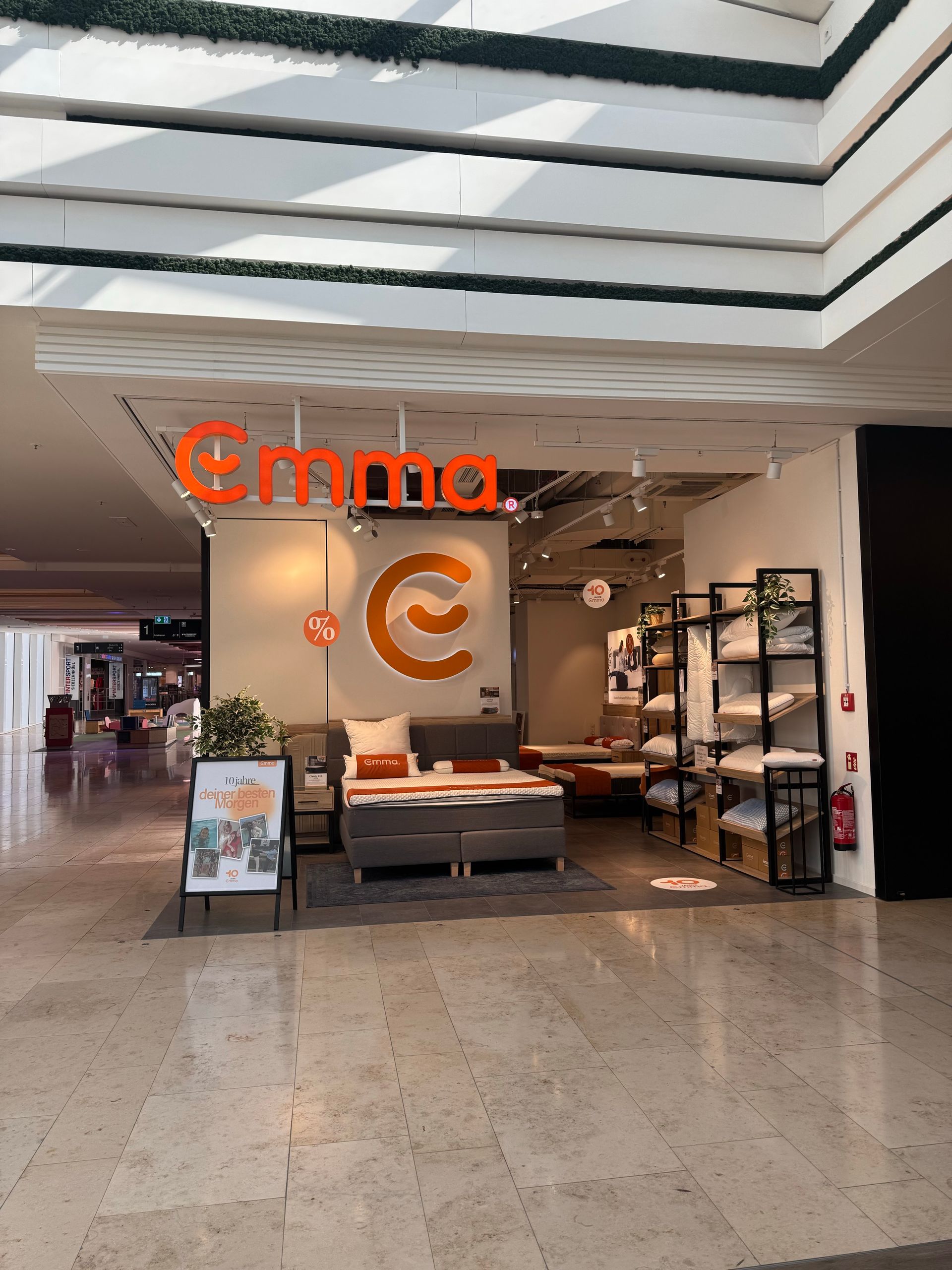 Emma Store München – der Ladenbereich mit orangefarbenem Emma-Logo, gemütlicher Möblierung und Produkten im Einkaufszentrum.
