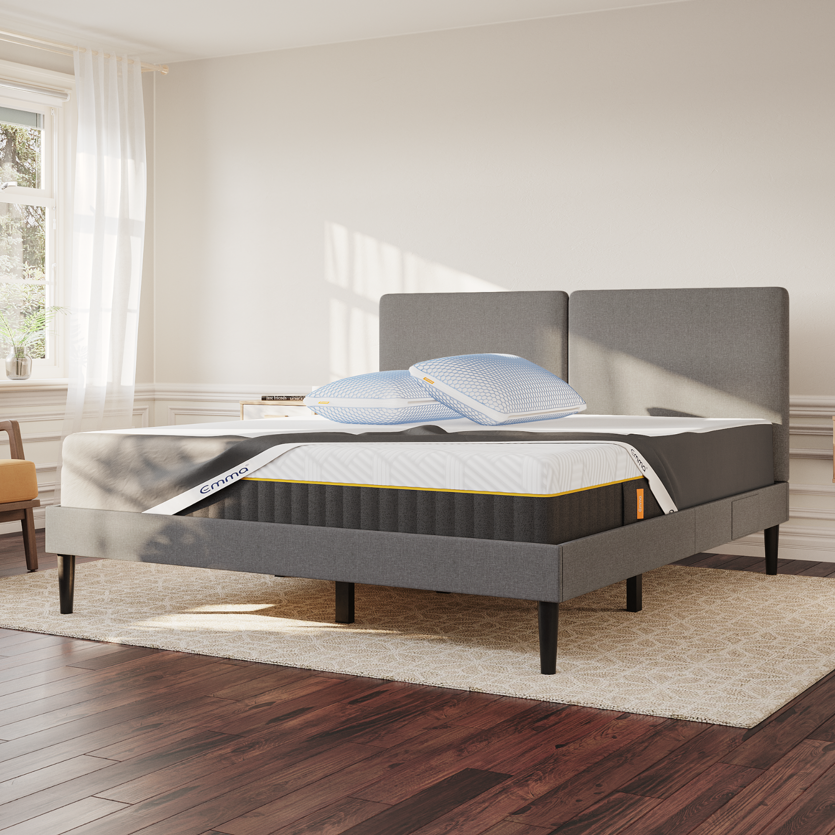 Chambre avec un lit gris et des pieds noirs. Le matelas est recouvert d’un protège-matelas et deux oreillers sont posés dessus.